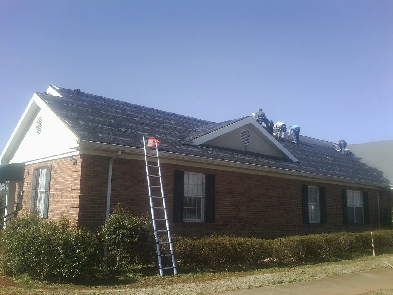Crew tearing shingles off a brick ranch roof with a ladder set — Emergency Roof Repair work by our crew in Mechanicstown