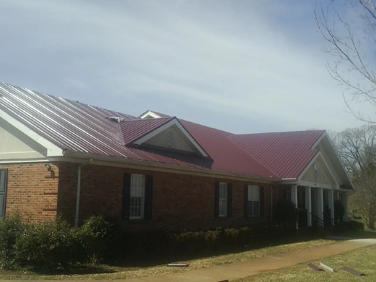 Red metal roof with gabled entries on a long brick building, from a Hail Damage Roof Repair job in Mechanicstown