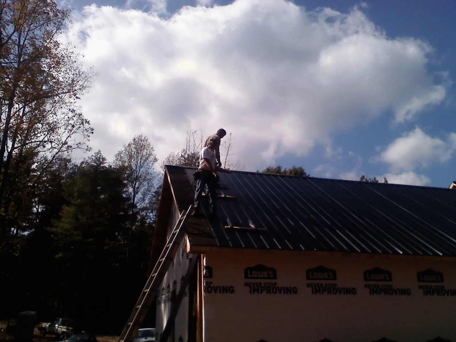 Roofer fastening dark metal panels high against a cloudy sky, from a Roof Inspection job in Mechanicstown