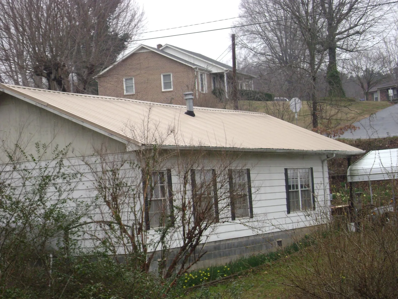 Tan metal roof on a white sided house set into a hillside — Commercial Roofing by Roofing Brothers in Mechanicstown